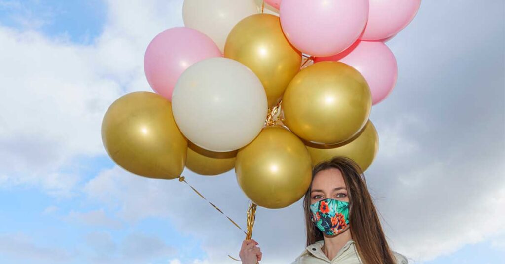 girl wearing mask holding balloons